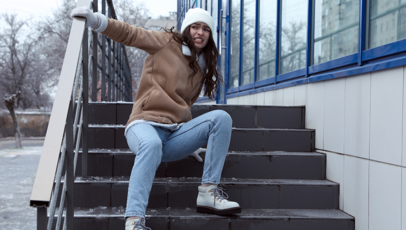 A young woman falls on slippery stairs covered with ice outdoors.