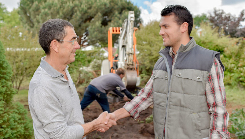 Two smiling men shake hands at a construction site