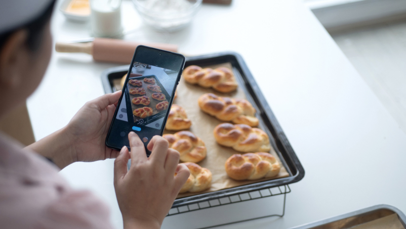 A baker uses a smartphone to take photos of freshly made bread to use on social media.